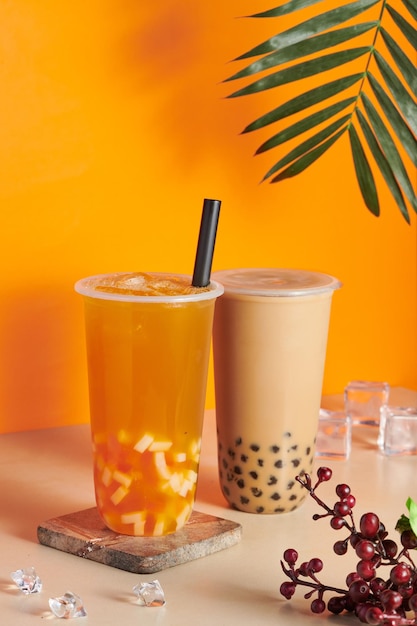Пластиковые чашки, наполненные свежим и вкусным апельсиновым соком и чаем с пузырьковым молоком на столе