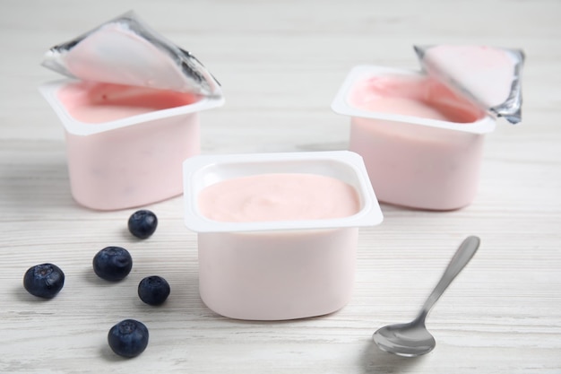 Photo plastic cups with tasty yogurts and blueberries on white wooden table