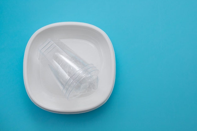 Пластиковая тарелка и пластиковый стаканчик на синем бумажном фоне