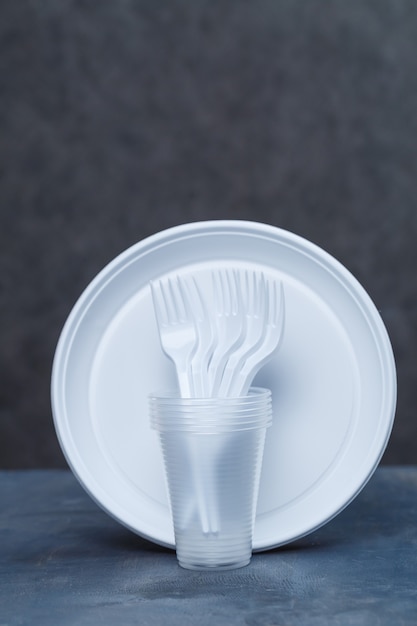 Plastic dishes, disposable tableware, plates, glasses, spoons, forks on a gray background. Caring for the environment. The problem is recycling. Reuse, safe planet, environmental concept.