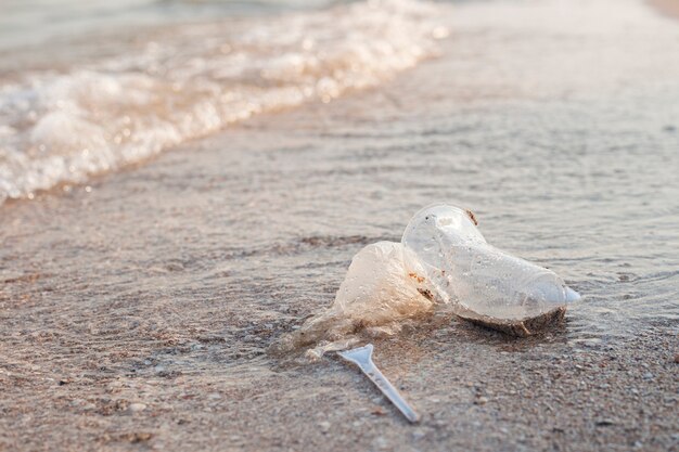 Plastic dishes and a plastic bag on the background of a sandy\
beach.