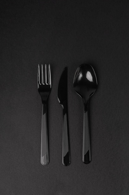 Plastic disposable black knife, spoon and fork on a dark background