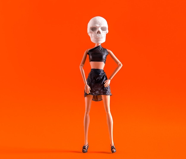 Photo plastic doll with skull for head dressed in black leather top and skirt on orange background