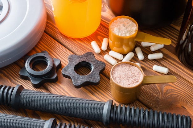 Plastic dumbbell and sports nutrition shaker on wooden background