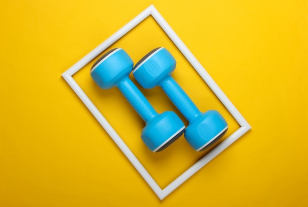 Photo plastic dumbbell on yellow surface with white frame