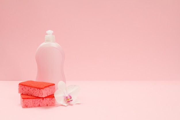 Plastic fles afwasmiddel sponzen en een orchideebloem op de roze achtergrond