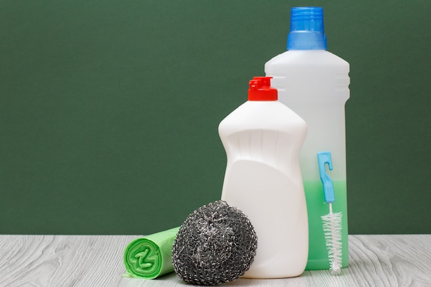 Plastic flessen afwasmiddel, wasmiddel voor magnetrons en fornuizen, borstel, metalen spons en vuilniszakken op groene achtergrond. Was- en schoonmaakconcept.