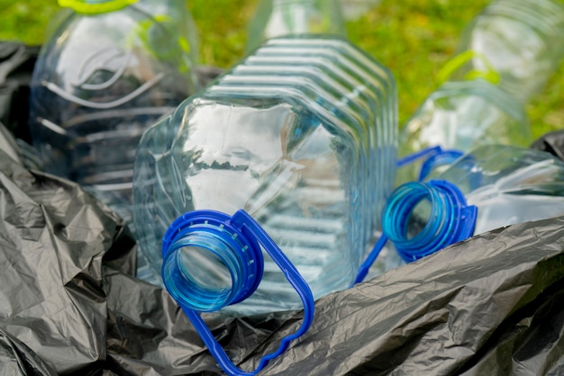 Plastic flessen in een zwarte plastic vuilniszak op een grasachtergrond.