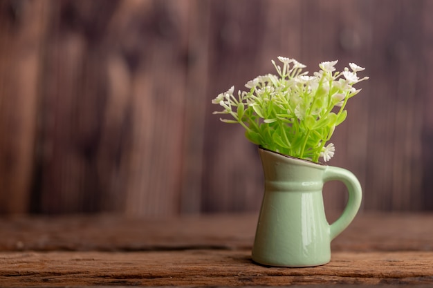 La plastica fiorisce in un posto verde della piastrella di ceramica della brocca sulla vecchia tavola di legno