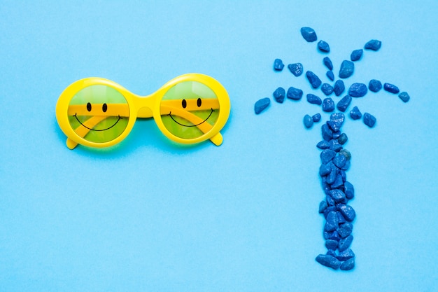 Plastic gele zonnebril met geschilderde ogen en een glimlach op de bril en decoratieve blauwe palmvormige stenen