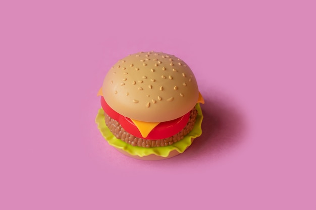 Plastic hamburger, salade, tomaat, op een roze achtergrond Exemplaarruimte