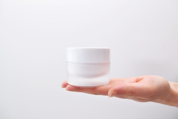 Plastic jar of cream in a female hand isolated on white. Professional cosmetics to restore skin youth, anti-aging cream. Skin care concept. 