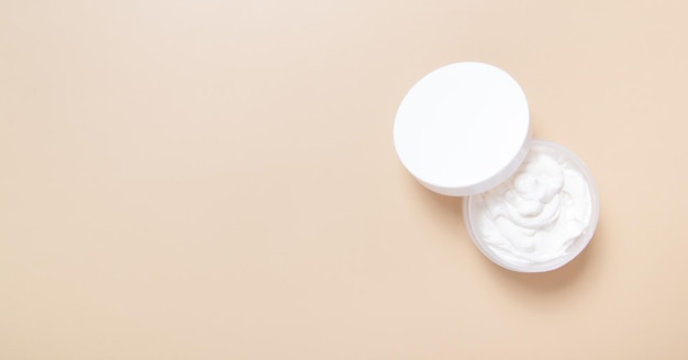 Plastic jar with white lid with cream on a beige background