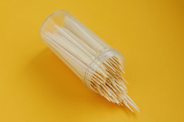 Plastic jar with wooden bamboo toothpicks lies on a yellow background