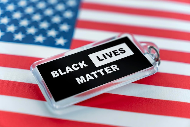 A plastic keychain with the symbol of the BLM movement black lives matter lying on the background of the American flag