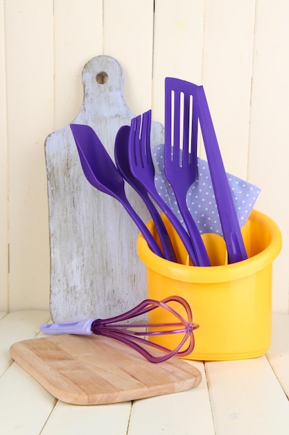 Plastic kitchen utensils in cup on wooden table