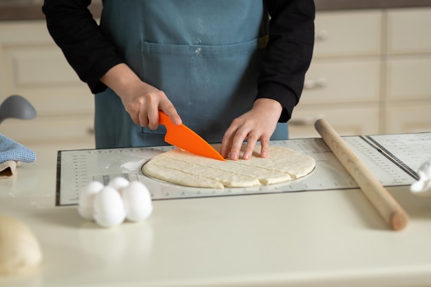 A plastic knife in the chef's hand cuts the rolled out pastry dough