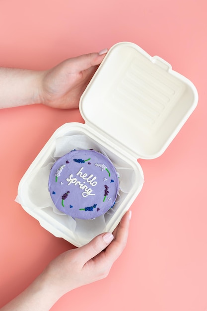 Plastic lunchbox met heerlijke bento cake Hallo lente in vrouwelijke handen op een roze achtergrond bovenaanzicht