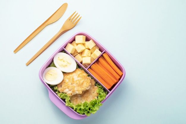 青い背景にフォークとナイフが付いているプラスチック製のお弁当箱。コピースペース