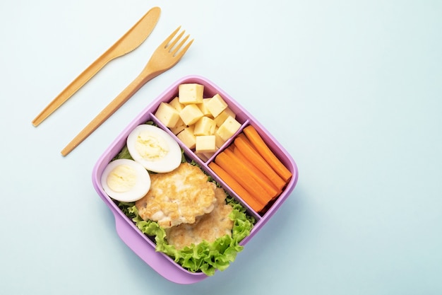 Plastic lunchbox with fork and knife on blue background. Copy space