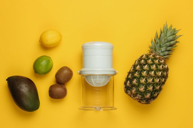 Plastic manual juicer  and tropical fruits on yellow background. Healthy food concept. Freshly squeezed juices. Top view