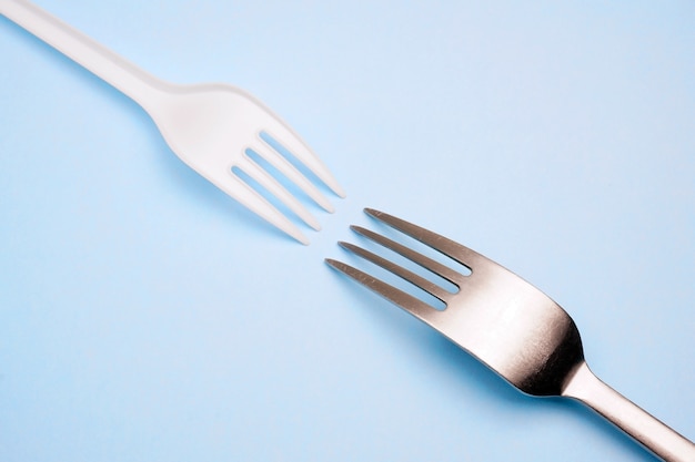 Plastic and metal fork on blue background. Creative minimal concept