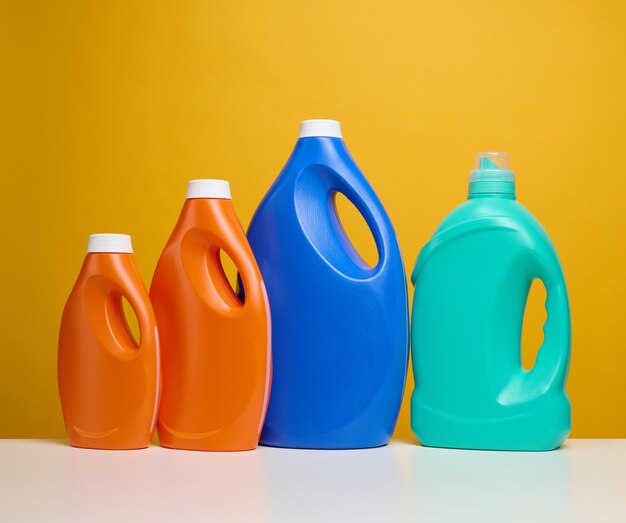 Plastic orange and blue large bottles with liquid detergent stand on a white table yellow background