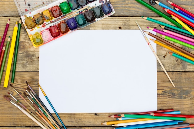 Plastic paint palette with paint and brushes on wooden table