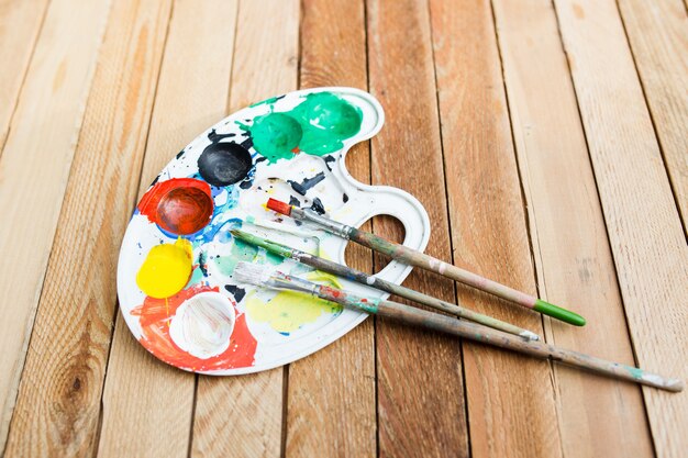 Plastic paint palette with paint and brushes on wooden table