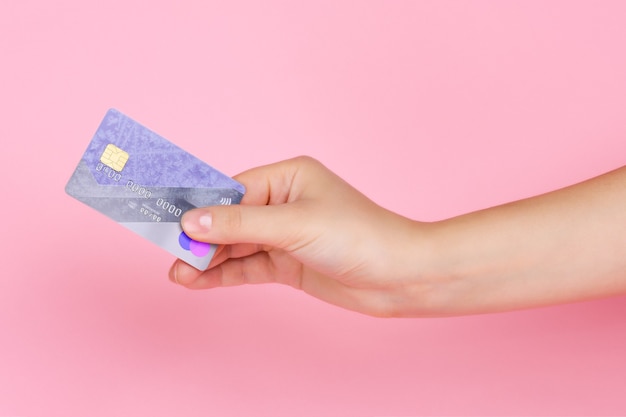 Plastic payment card in a female hand, on a light pink