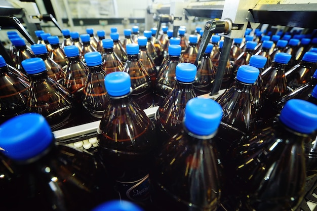 Plastic PET bottles made of yellow plastic with blue lids with beer or sweet drinks on a conveyor belt in the background of the factory. Industrial food production of beverages.