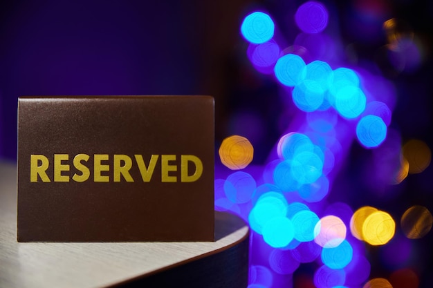 Plastic plaque with the inscription Reserved on the restaurant table on backdrop of colorful lights