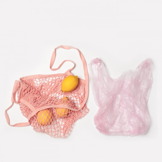 Plastic plastic zak en roze katoenen netzak milieuvriendelijk. Het concept van vergelijking. Zonder plastic, geen afval. Lichtgrijze achtergrond met kopie ruimte. Fruit, citroenen. Niemand
