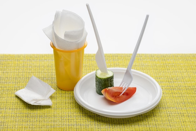 Plastic plate with pieces of tomato and cucumber. Knife, fork and glass with napkins, studio shot.