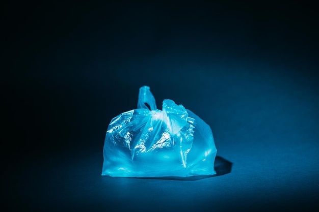 Plastic pollution. Ecology problem. Nature conservation. Environmental protection. Blue cellophane bag filled with air in spotlight isolated on dark copy space background.