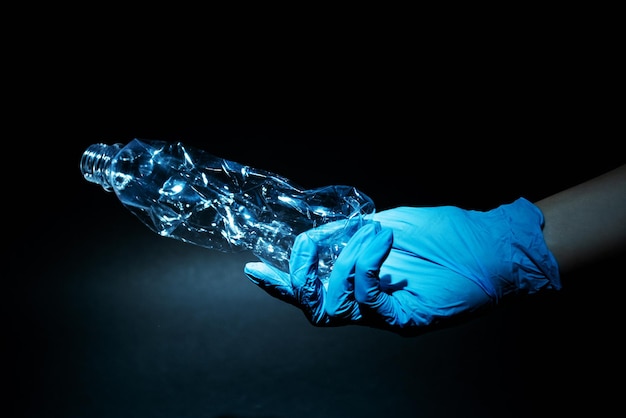 Plastic recycling Garbage management Environmental protection Volunteer hand in blue glove holding used crushed bottle isolated on dark empty space background