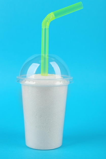 Photo plastic smoothie cup with granulated sugar and cocktail tube on blue background