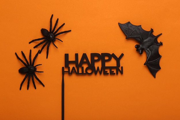 Plastic spinnen met vleermuis en het woord happy halloween op oranje achtergrond Halloween decor Top view