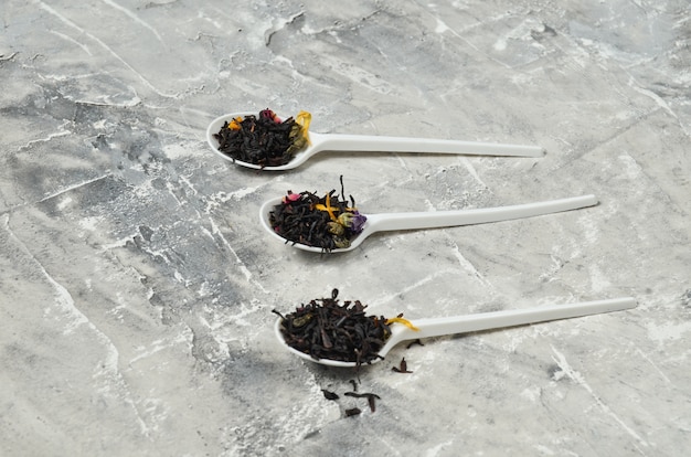 Plastic spoons with dry tea leaves on a gray concrete surface