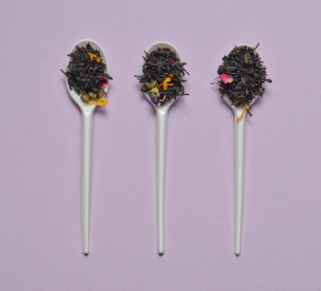 Cucchiai di plastica con foglie di tè secche su una superficie viola