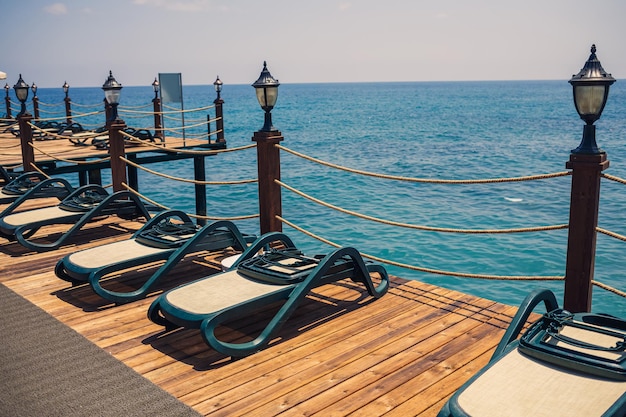 Plastic sun loungers stand in a row on the pier on the beach by the sea