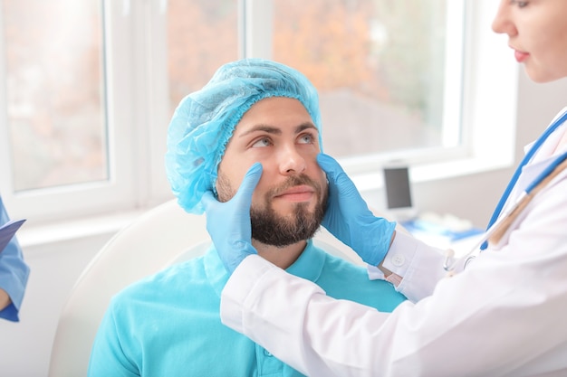 Plastic surgeon examining young man's face prior to operation in clinic