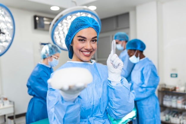Plastic surgeon woman holding silicon breast implants and a scalpel in surgery room interior