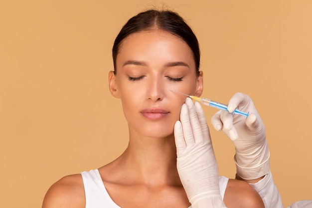 Plastic surgery and beauty injection concept Attractive young woman receiving botox for wrinkles beige background