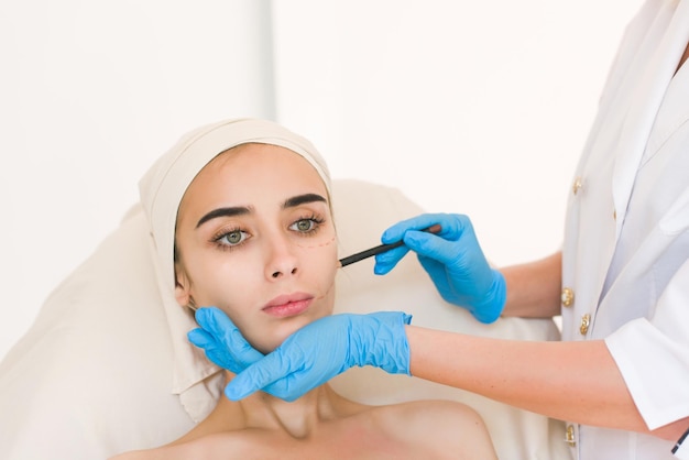 Plastic surgery concept. Hand in blue glove marking women face against white background.