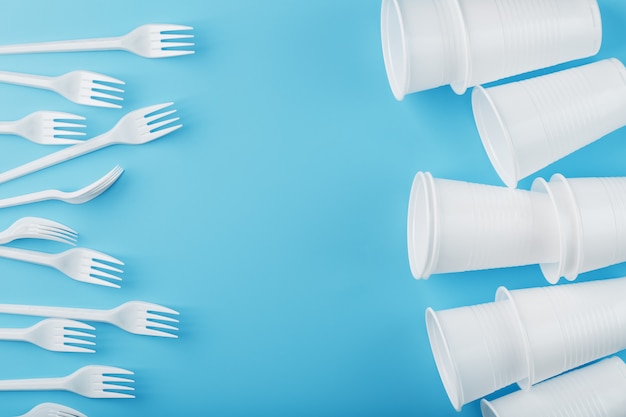 Photo plastic tableware on a blue wall. disposable forks and glasses with free space.