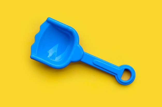 Plastic toy, shovel on yellow surface.