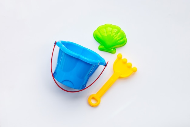 Plastic toys, shovel with bucket for sand on white surface.