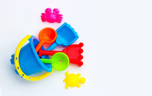 Plastic toys, shovels in bucket for sand on white surface.