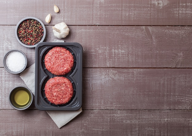 Plastic tray with raw minced homemade grill beef burgers with spices and herbs. Top view and.